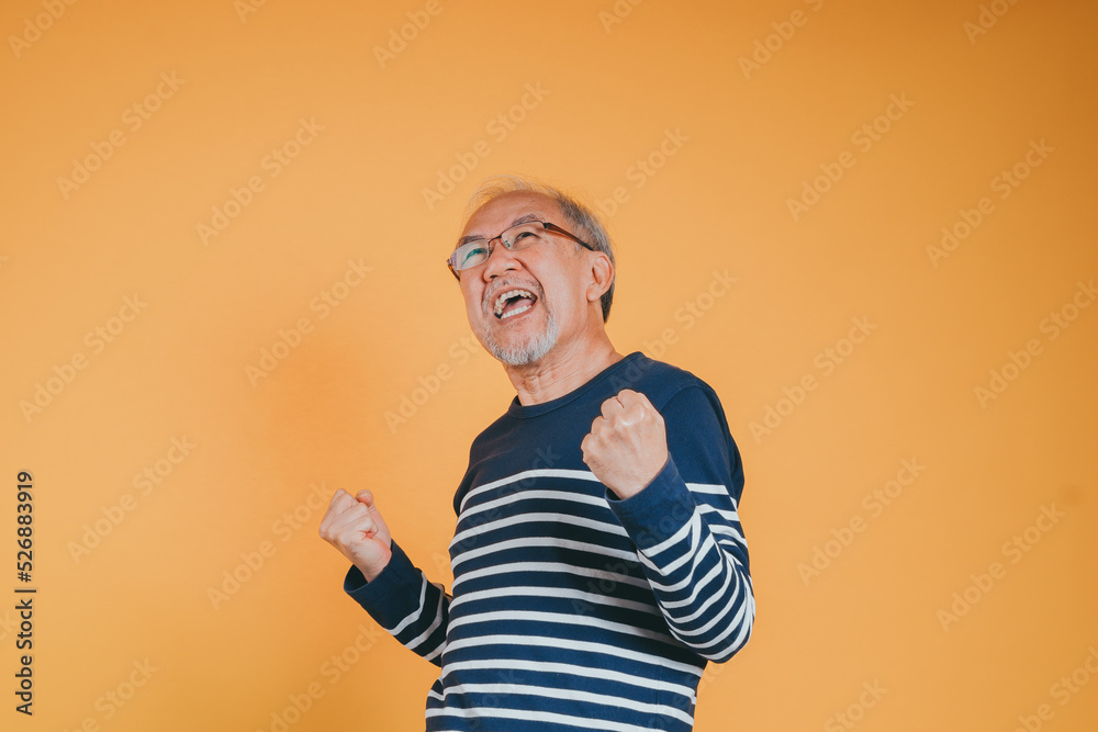 Excited glad expression of Senior elderly old man arms raised to celebrating victory success feeling, Happy Asian elder man with glasses yes like winner emotion on yellow background Excited glad expression of Senior elderly old man arms raised to celebrating victory success feeling, Happy Asian elder man with glasses yes like winner emotion on yellow background