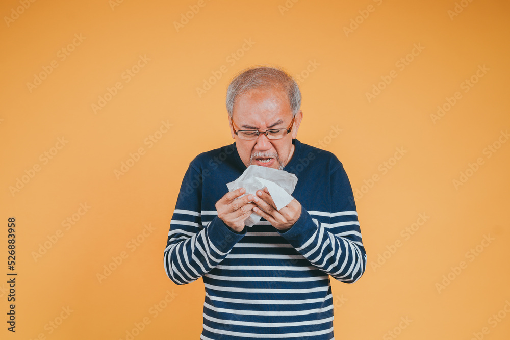 Senior old man sneezing with tissue, Asian elderly man sick, cold having fever and flu sinus from sickness virus problem use tissue, pensioner unwell on the yellow background Senior old man sneezing with tissue, Asian elderly man sick, cold having fever and flu sinus from sickness virus problem use tissue, pensioner unwell on the yellow background