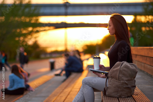 Young asian woman with coffee and book in the evening at sunset. outdoor city portrait