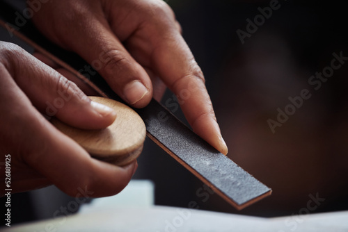 Macro shot of unrecognizable artisan sanding handmade leather piece in leatherworking shop, copy space