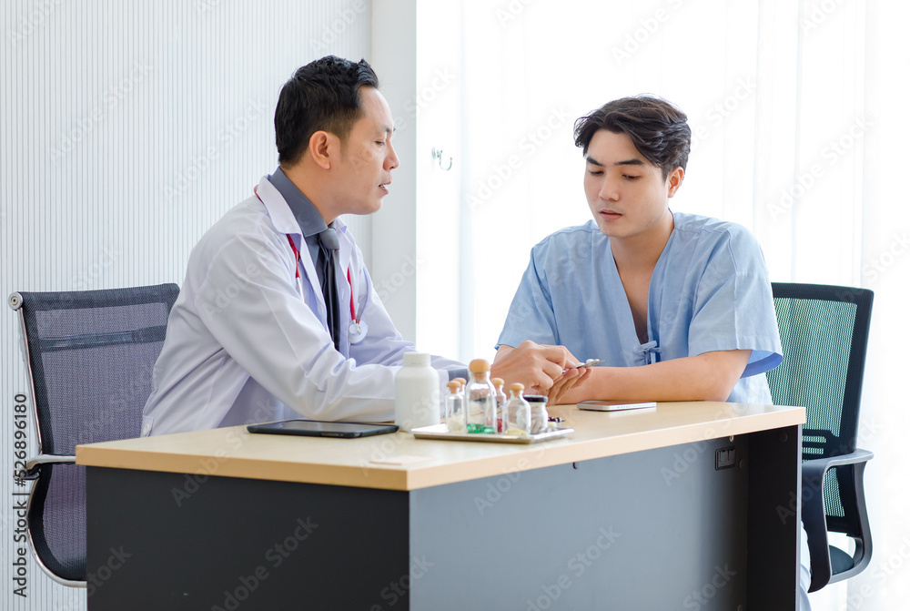 Asian male patient in blue hospital uniform sitting on wheelchair meeting discussing consulting with professional successful middle aged doctor in white lab coat with stethoscope about injury symptom Asian male patient in blue hospital uniform sitting on wheelchair meeting discussing consulting with professional successful middle aged doctor in white lab coat with stethoscope about injury symptom