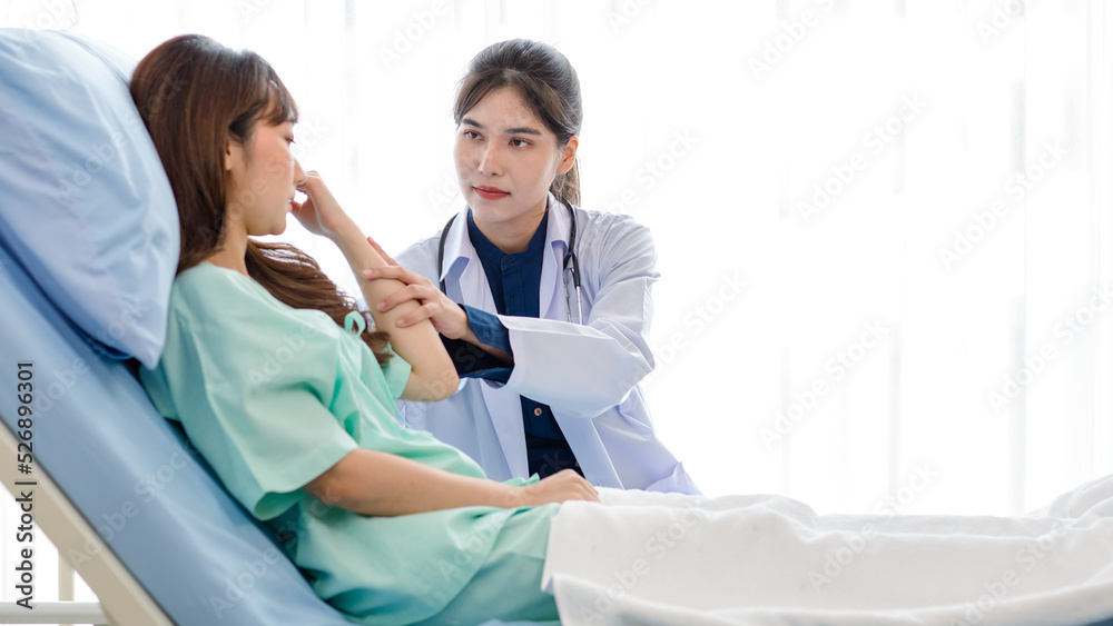 Fototapeta premium Asian young professional female practitioner doctor in white lab coat with stethoscope holding touching checking monitoring patient injury arm and muscle while laying down on bed in hospital wardroom