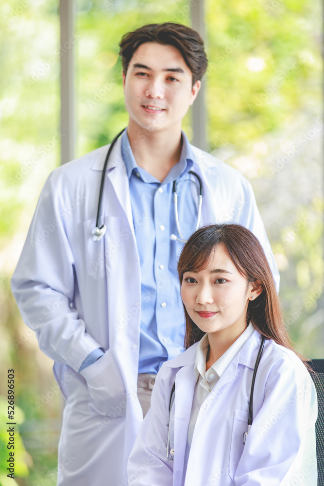 Asian young cheerful successful professional male and female internship practitioner doctors in white lab coat uniform with stethoscope smiling posing standing and sitting together in hospital lobby Asian young cheerful successful professional male and female internship practitioner doctors in white lab coat uniform with stethoscope smiling posing standing and sitting together in hospital lobby