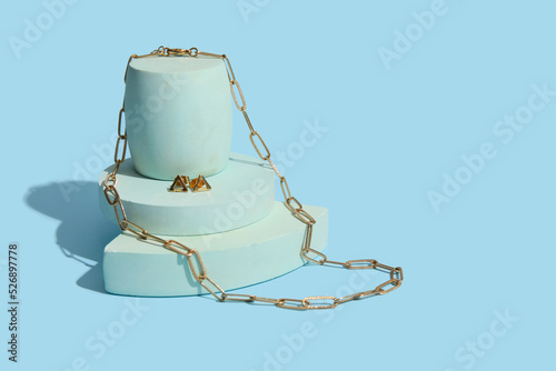 Showcase pedestal with trendy necklace and earrings on blue background