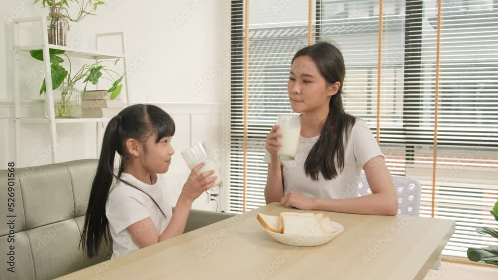A Healthy Asian Thai family, little daughter, and young mother drink fresh white milk in glass and bread joy together at a dining table in morning, wellness nutrition home breakfast meal lifestyle. A Healthy Asian Thai family, little daughter, and young mother drink fresh white milk in glass and bread joy together at a dining table in morning, wellness nutrition home breakfast meal lifestyle.