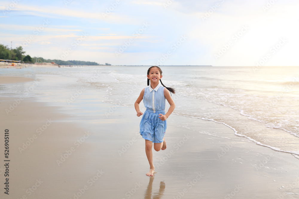 Cheerful Asian young girl child having fun running on tropical sand beach at sunrise.