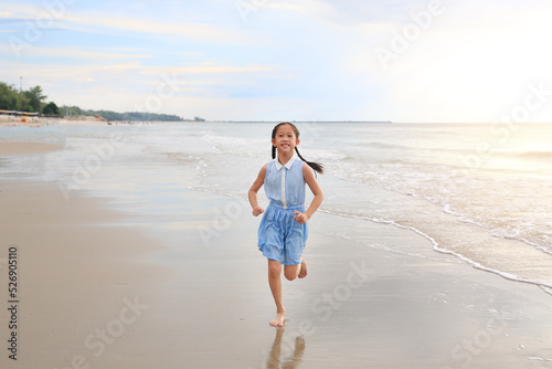 Cheerful Asian young girl child having fun running on tropical sand beach at sunrise.