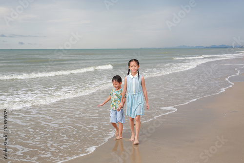 Asian girl child and little boy walking together on tropical sand beach. Happy family sister and brother enjoy in summer holiday.