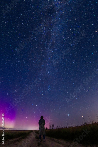 abstract night photo of a figure of a lonely person in a field under a starry sky and northern lights  starfall. Astrophotography
