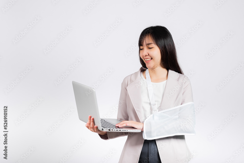 Asian business woman confident smiling broken arm after accident and wear arm splint for treatment but still have to work she hold laptop computer studio isolated on white background,copy space Asian business woman confident smiling broken arm after accident and wear arm splint for treatment but still have to work she hold laptop computer studio isolated on white background,copy space