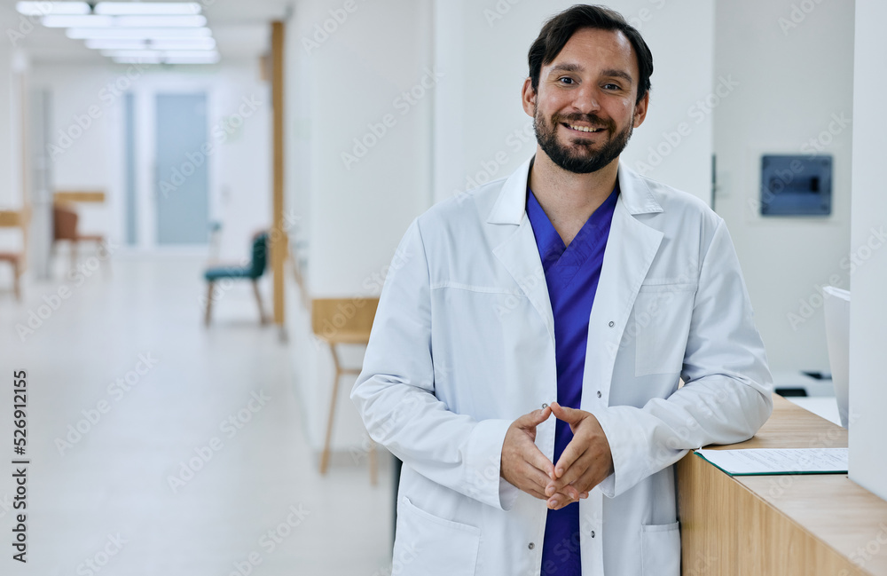 Friendly male general practitioner wearing medical uniform standing in modern medical clinic, portrait. Doctor occupation