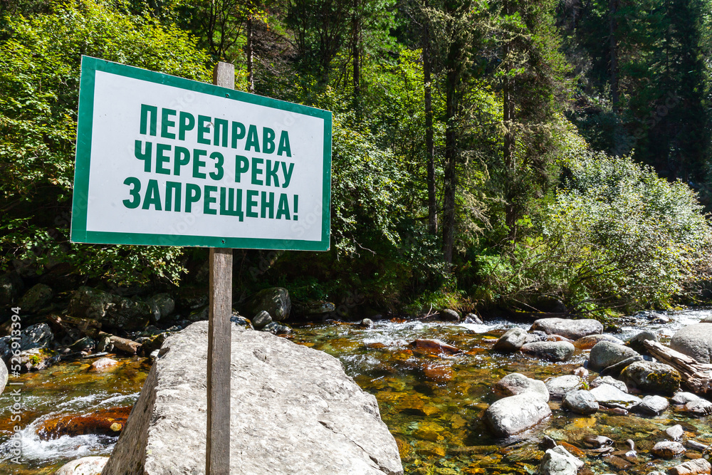 White wooden banner with green text mounted on a river coast.