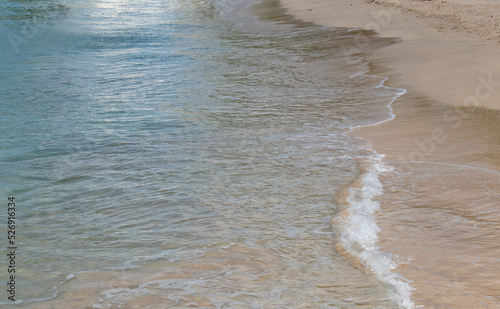 Ocean tide rolling in against a white sand beach on a summer day.