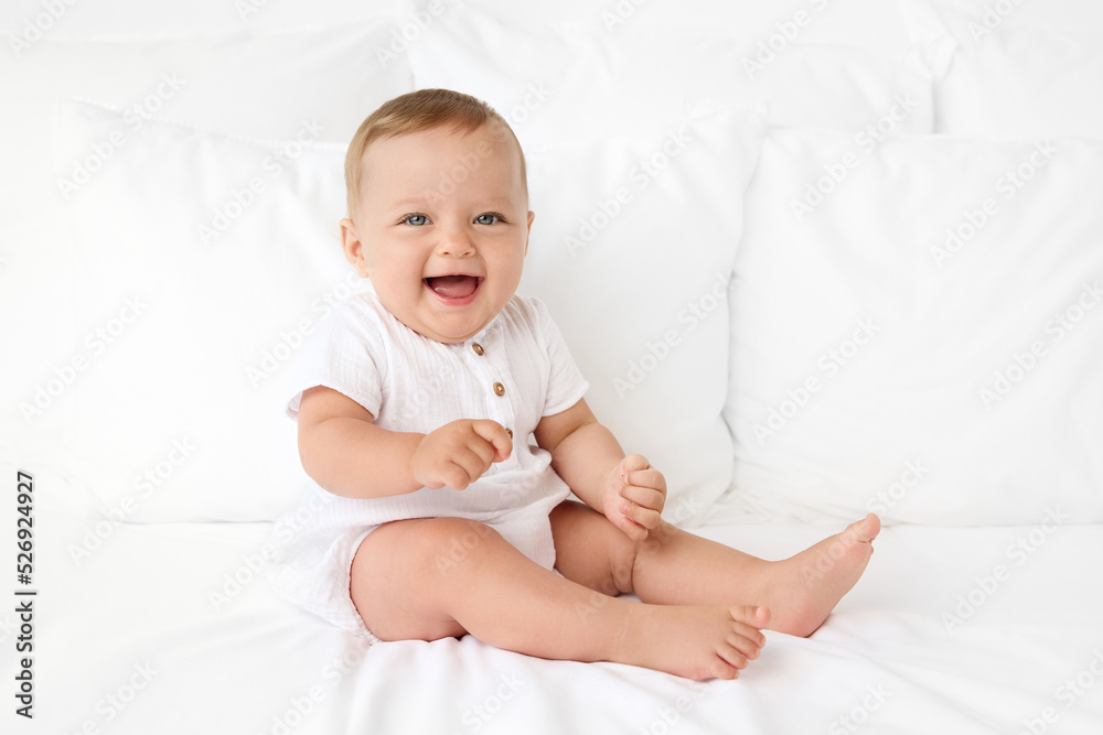 Laughing blue-eyed baby sitting on white bed