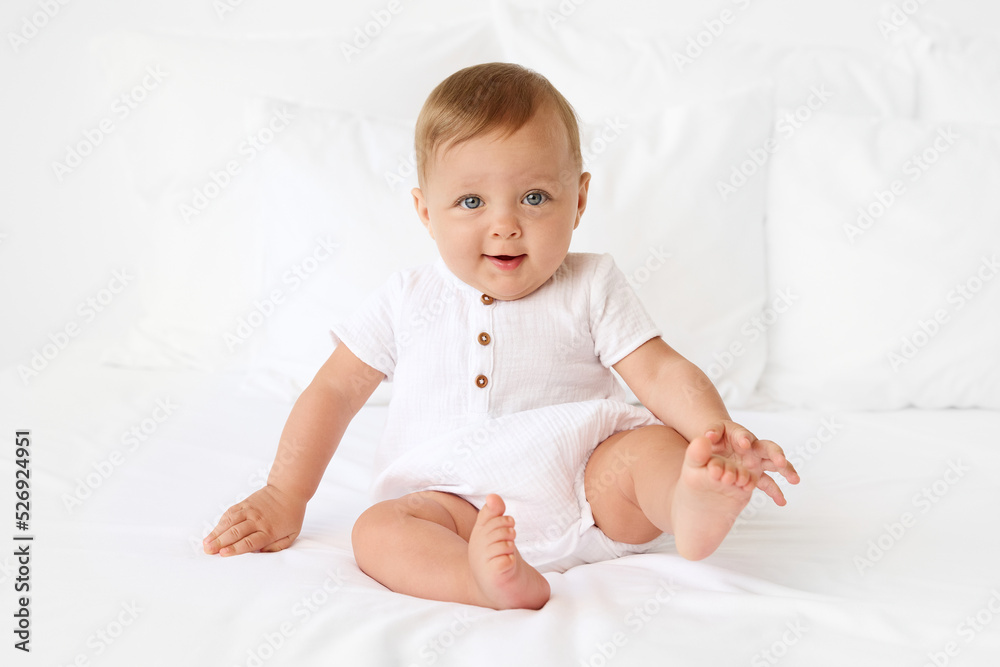 Cute baby sitting on white bed with foot in the air Cute baby sitting on white bed with foot in the air