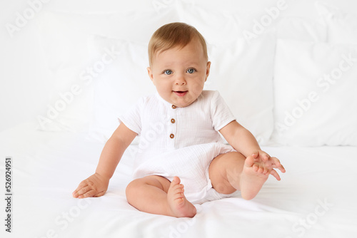 Cute baby sitting on white bed with foot in the air