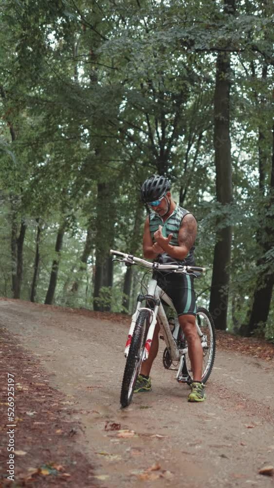 An adult sportsman takes  his pulse measurement in the forest after a hard bike ride on a muddy road in nature