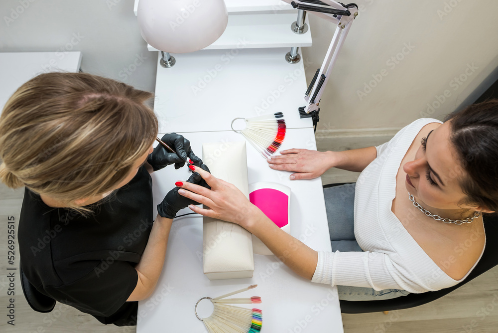 The manicurist covers the client's nails with red varnish. Manicure in a beauty salon.