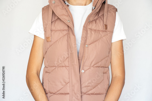 A girl in a white T-shirt and a pink warm vest stands on a white background, fashionable warm women's clothing, autumn vest, clothing