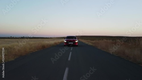 Low POV : Shiny red vehicle drives on country road at dawn, headlights photo