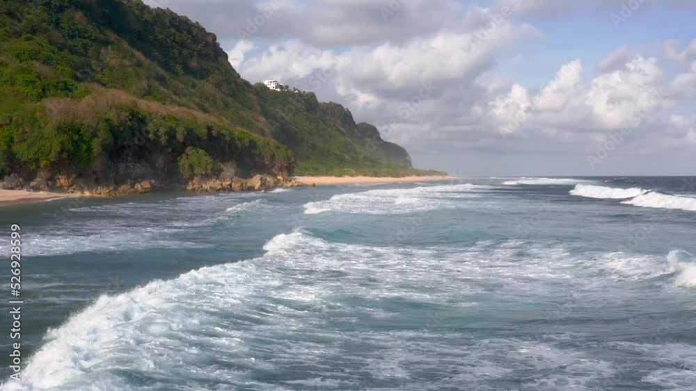 Aerial view of low tides moving towards the shore of beach surrounded by huge green cliffs. Aerial view of low tides moving towards the shore of beach surrounded by huge green cliffs.