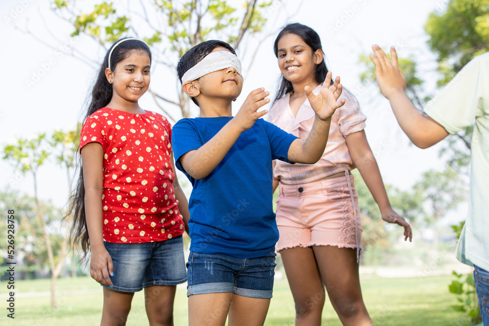 Fototapeta premium Group of happy Indian kids playing blindfold game in summer park, Playful asian children in the garden. Childhood. 