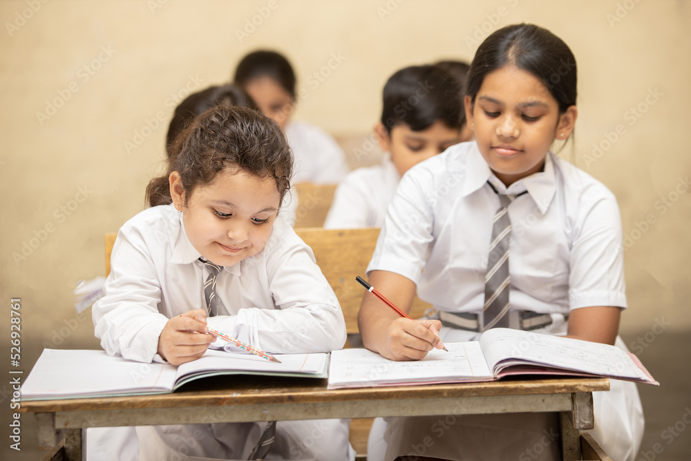 Indian elementary school students sitting at desk in classroom with writing in notebook with pencil, Examination and test, Girl Education concept. Indian elementary school students sitting at desk in classroom with writing in notebook with pencil, Examination and test, Girl Education concept.