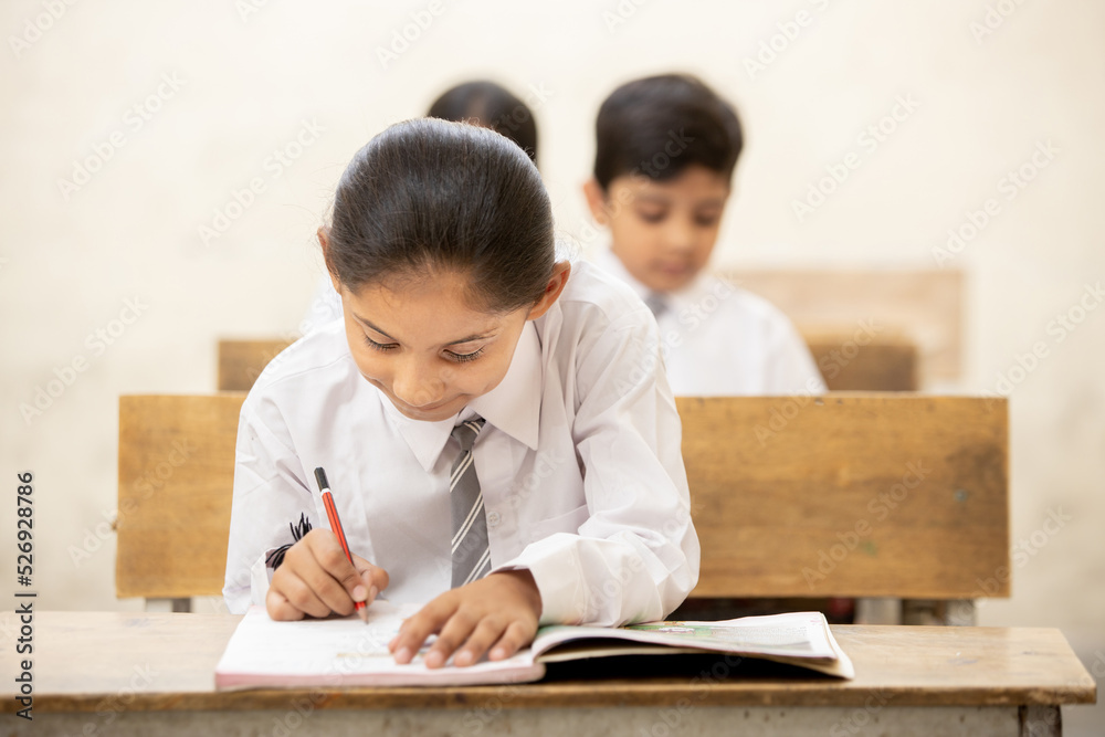 Indian schoolboy sitting at desk in classroom, group of school kids with pens and notebooks writing test Elementary school, Education concept. Indian schoolboy sitting at desk in classroom, group of school kids with pens and notebooks writing test Elementary school, Education concept.