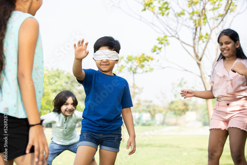 Group of happy Indian kids playing blindfold game outdoors in park, Playful asian children in the garden.