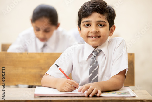 Portrait of happy indian school sitting at desk in classroom, school kids with pens and notebooks writing test Elementary school, Education concept. photo