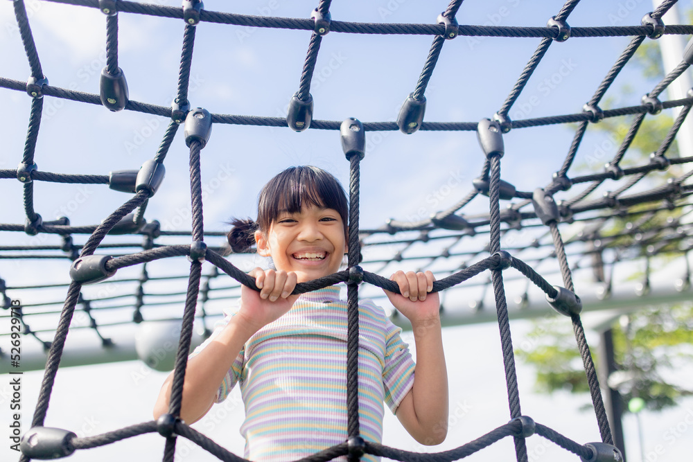 Kid girl doing exercises climbing tightrope at kindergarten or elementary school. Children's sport and fitness concept.