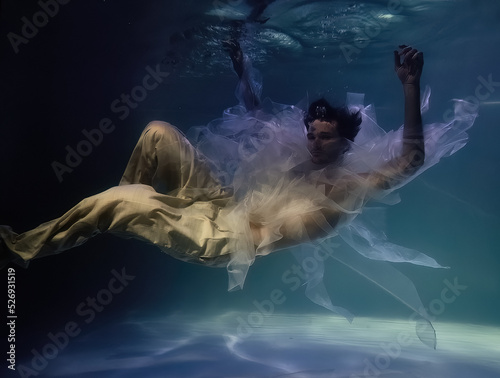 young man in white ribbons and trousers underwater in the pool on a dark background