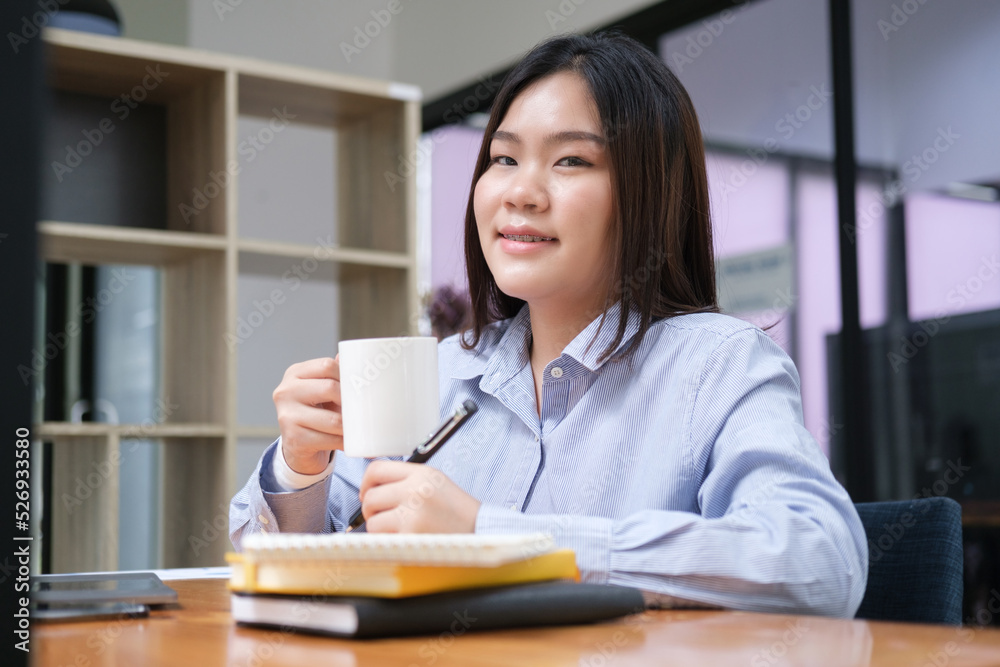 Happy young businesswoman drinking coffee and working at bright office.. Happy young businesswoman drinking coffee and working at bright office..