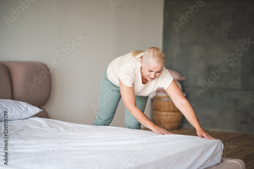 A blonde mid aged woman holding apillow and making bed
