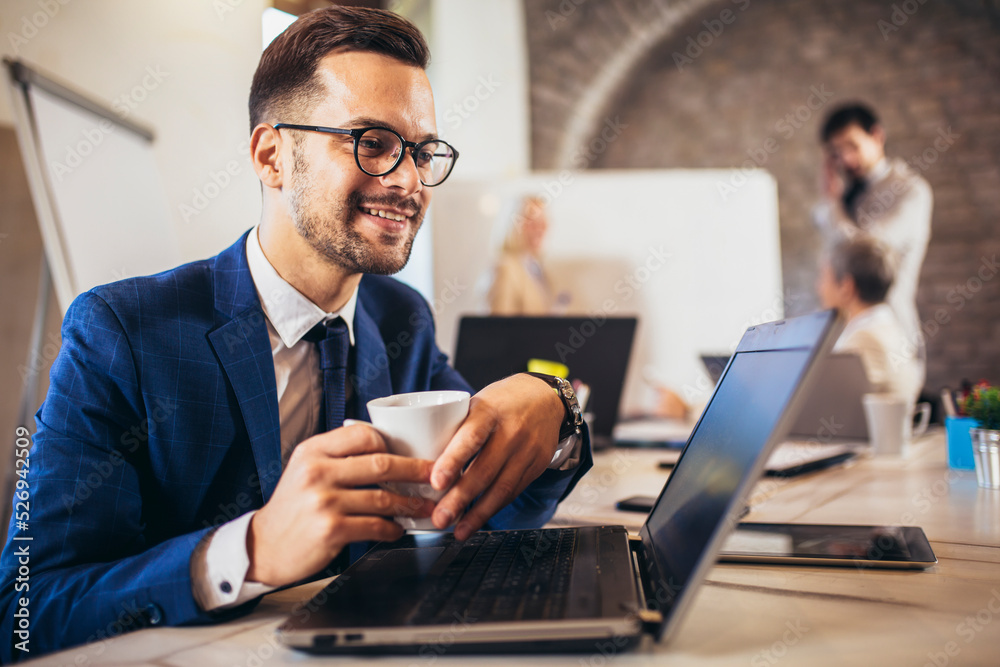 Happy businessman using laptop with team discussing project in the background. Happy businessman using laptop with team discussing project in the background.