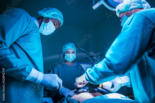 Team of surgeon doctor using defibrillator to give electrical shock to patient heart who is suffering from cardiac arrest in emergency surgical room for healthcare concept