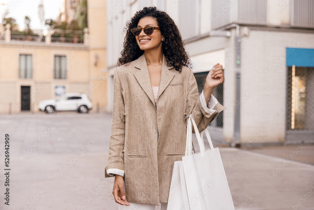 Positive young african girl in sunglasses looks away, stands on street with bag. Brunette wears business style of clothes. Concept stylish vacation. Positive young african girl in sunglasses looks away, stands on street with bag. Brunette wears business style of clothes. Concept stylish vacation.