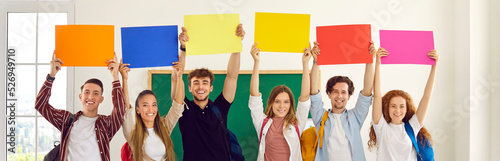 Group of happy diverse school or college students showing colorful mockup banners. Several smiling young people standing in row and holding up blank orange, blue, yellow, red and pink sheets of paper