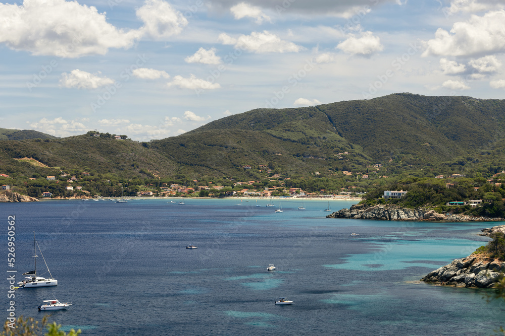 Spiaggia di Procchio and Spartia Beach, rare motor boats and yachts in turquoise water lagoons and a backdrop of densely forested coastal mountains. Island of Elba, Italy