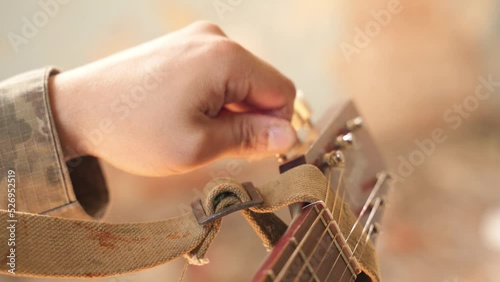 a soldier in camouflage tunes a guitar to play. military art and hobby. rest on duty after battle. a soldier prepares to sing and play the acoustic guitar