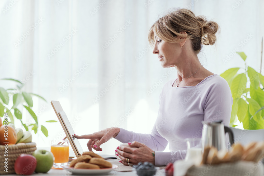 Mature woman having breakfast and using her tablet Mature woman having breakfast and using her tablet