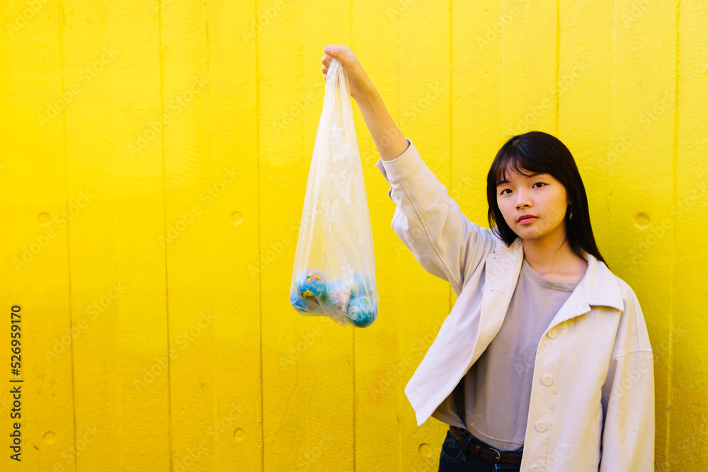 Young woman holding globes in polythene bag with hand raised in front of wall Young woman holding globes in polythene bag with hand raised in front of wall
