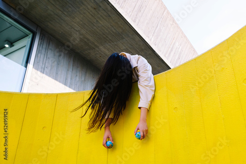 Unconscious young woman holding globes leaning on yellow wall photo
