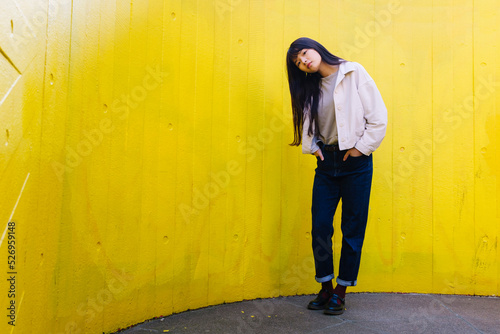 Young woman with head cocked standing in front of yellow wall photo