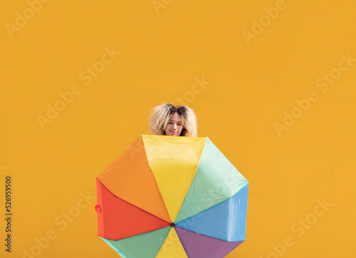 Smiling young woman with multi colored umbrella in front of yellow wall on sunny day photo