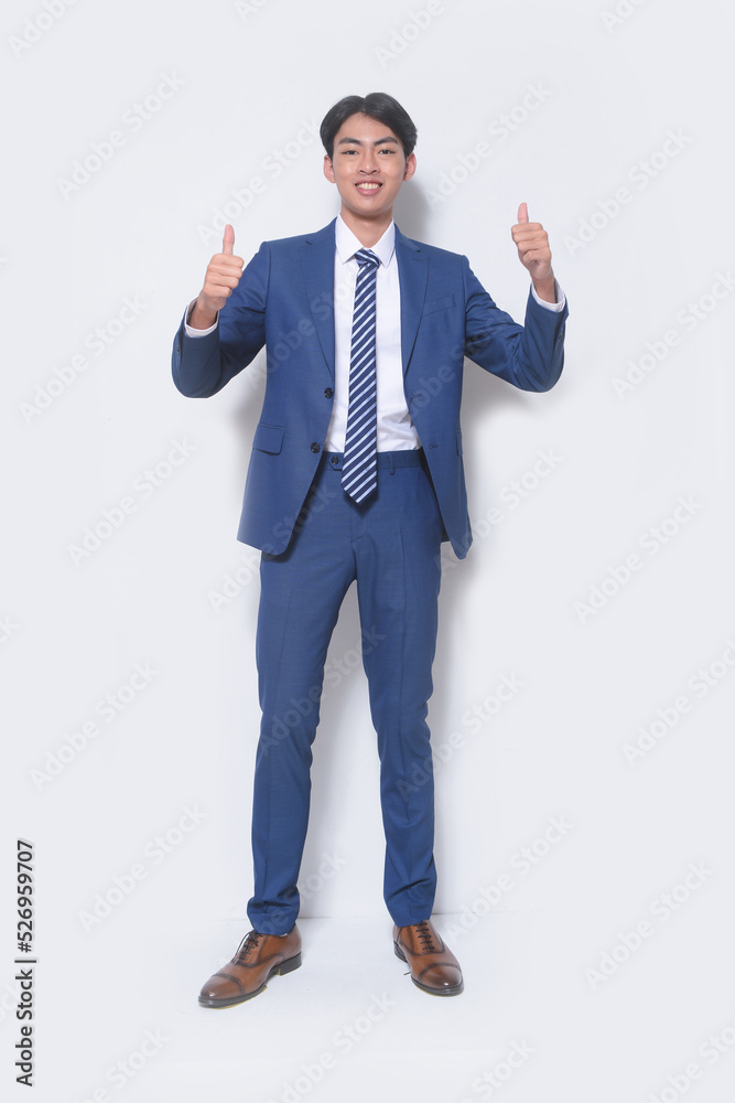Full body young businessman wearing suit, blue shirt with tie with hands, thumbs up standing in studio Full body young businessman wearing suit, blue shirt with tie with hands, thumbs up standing in studio