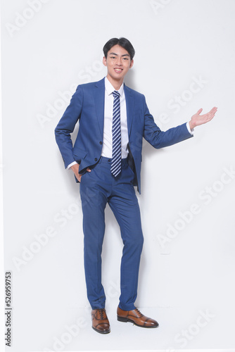 Full body young businessman wearing suit, blue shirt with tie with welcome gesture standing in studio