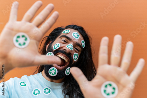 Hipster man with recycling stickers on face and palms shouting in front of wall photo
