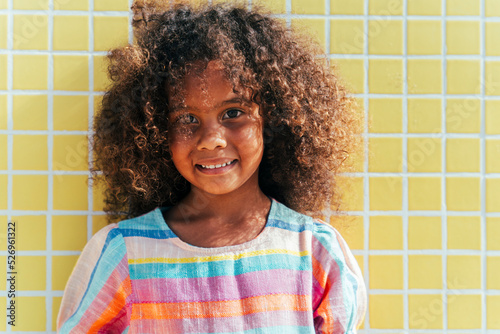 Smiling girl with curly hair in front of yellow wall