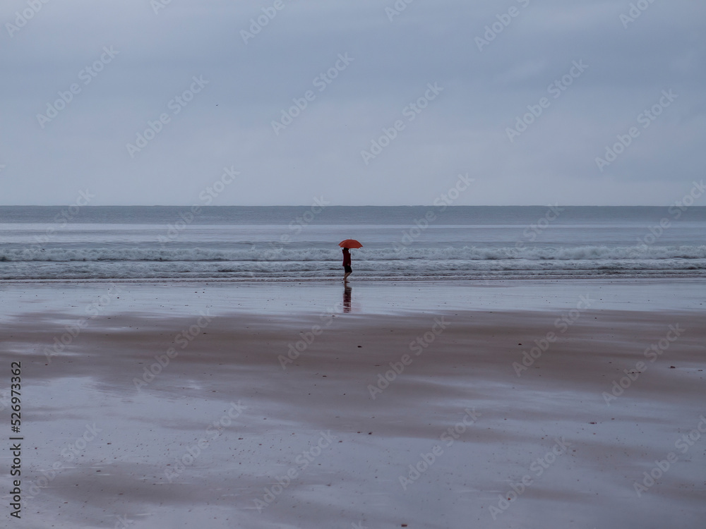 woman walking along the seashore with umbrella
